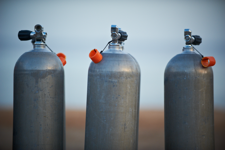 Trois bouteilles de plongée alignées, illustrant le concept de réduction de la consommation d'air en plongée