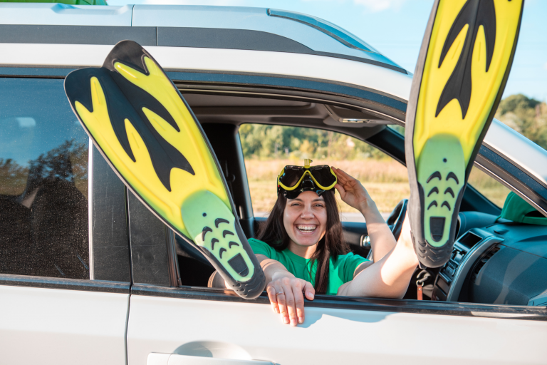 Entre deux mondes : une plongeuse joyeuse transforme sa voiture en caisson de décompression, palmes aux pieds.