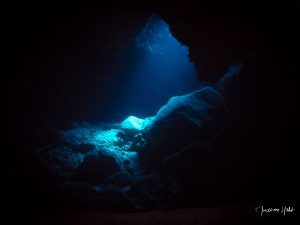 Ambiance lumineuse spectaculaire dans une grotte près de Los Gigantes, Tenerife, où un puits de lumière illumine une roche majestueuse.