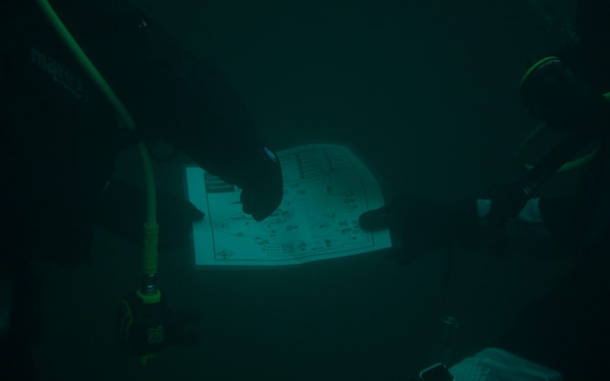 Navigation sous-marine : Maxime HIBLOT capture le moment où deux plongeurs en formation examinent une carte du site, soulignant l'importance de l'autonomie en plongée.